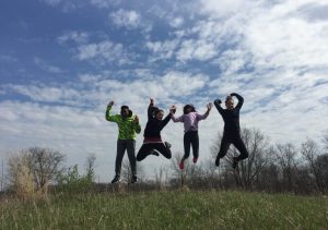 People jumping while on a hill under a cloudy and blue sky