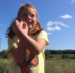Photo of little girl holding a monarch butterfly that has been tagged on the monarch tagging Field Trip.