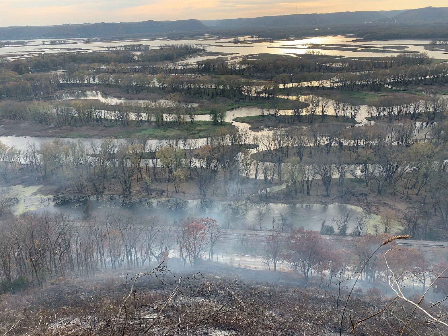  In the north unit of Rush Creek SNA, one of the remnant prairie openings smokes after a fall prescribed burn overlooking the Mississippi River. Prescribed fire is a vital tool in bluff prairie management. Photo: Justin Nooker, Wisconsin DNR.