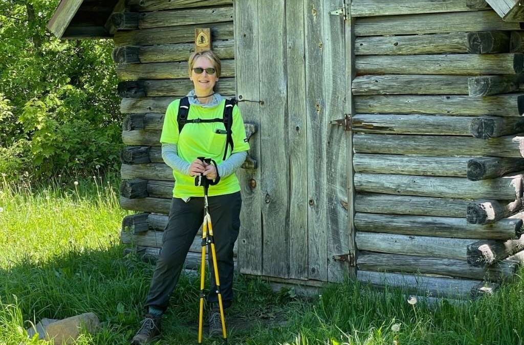 New Director of Philanthropy Marta Weldon wearing hiking gear stands in front of a log cabin.