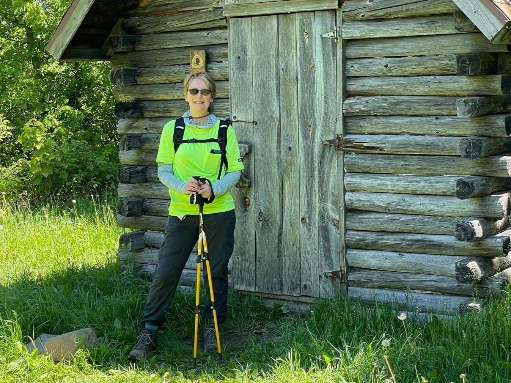 New Director of Philanthropy Marta Weldon wearing hiking gear stands in front of a log cabin.