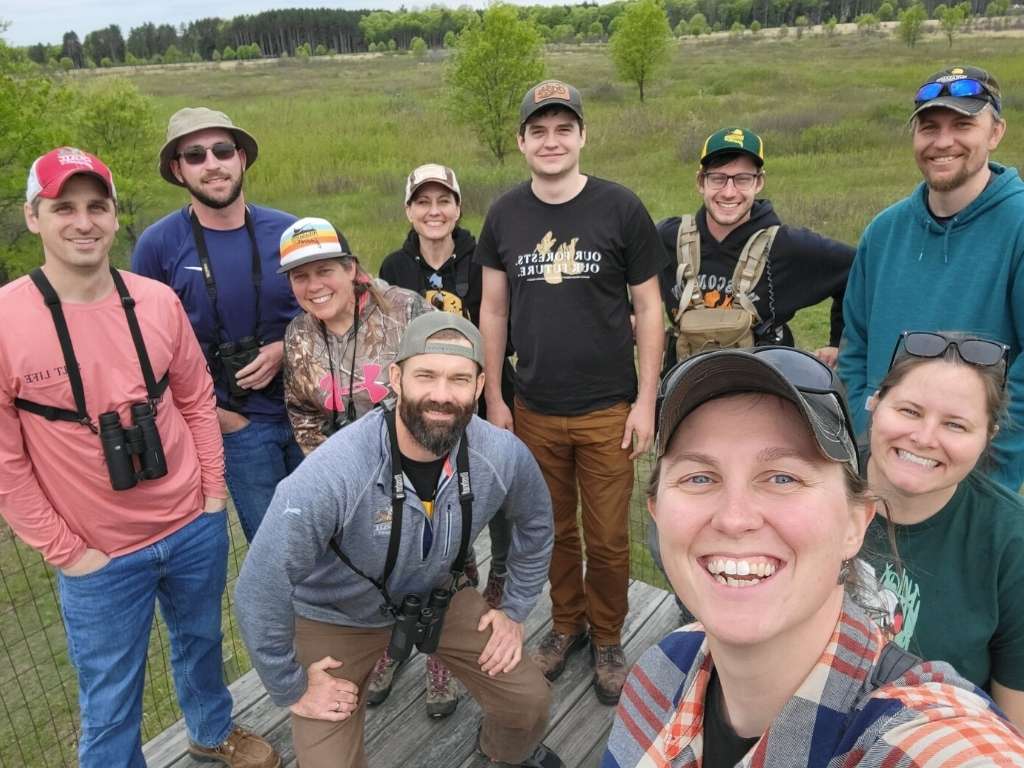 A group of young people with binoculars smile while birding at a field