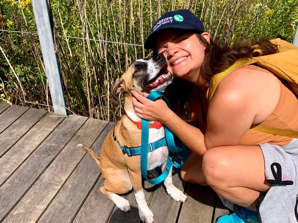 Luna, Emma's light brown and white puppy, giving her a kiss on the cheek while on a viewing platform looking over a prairie.