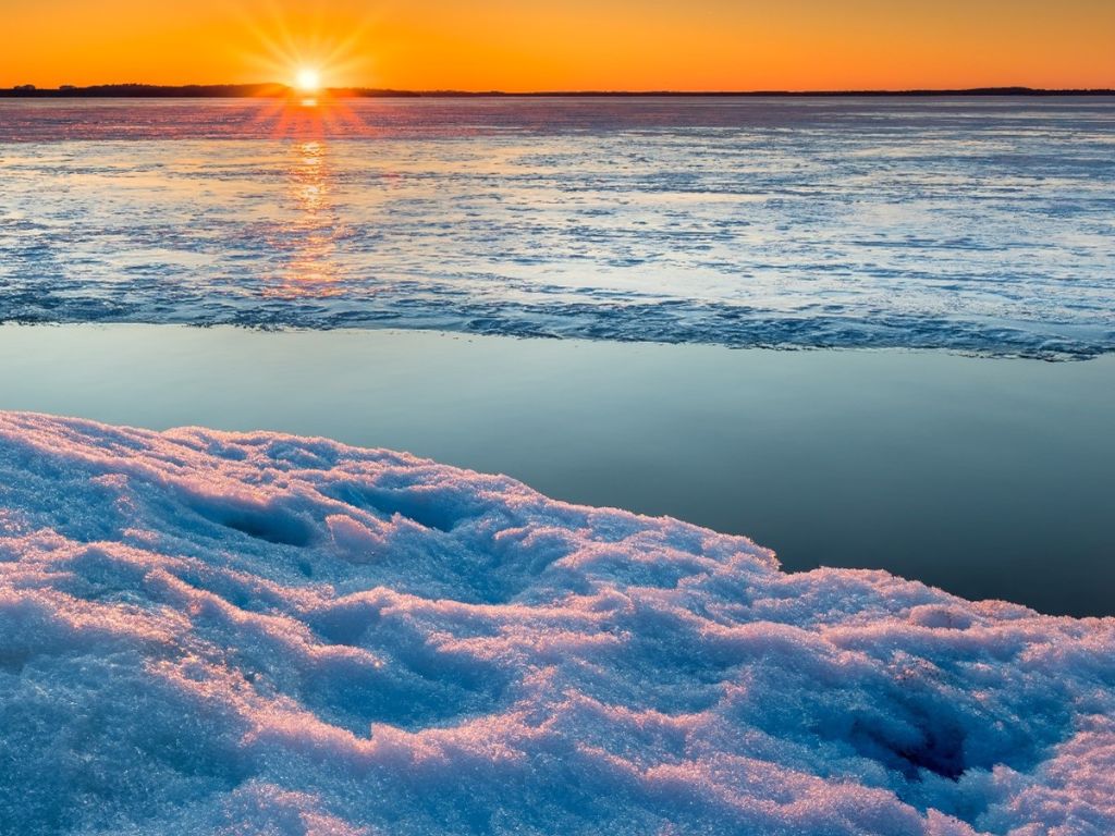 Climate Resiliency - orange sun and sky reflects on half frozen lake with snow and ice in the foreground