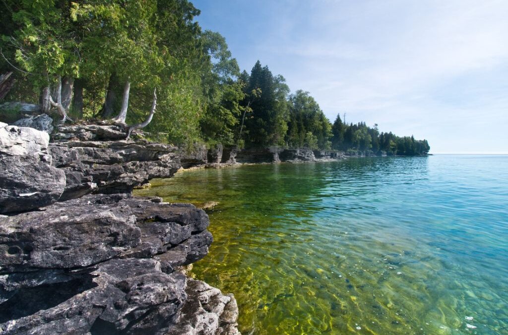 A rocky tree-lined shoreline with clear blue-green water in Door County, Wisconsin