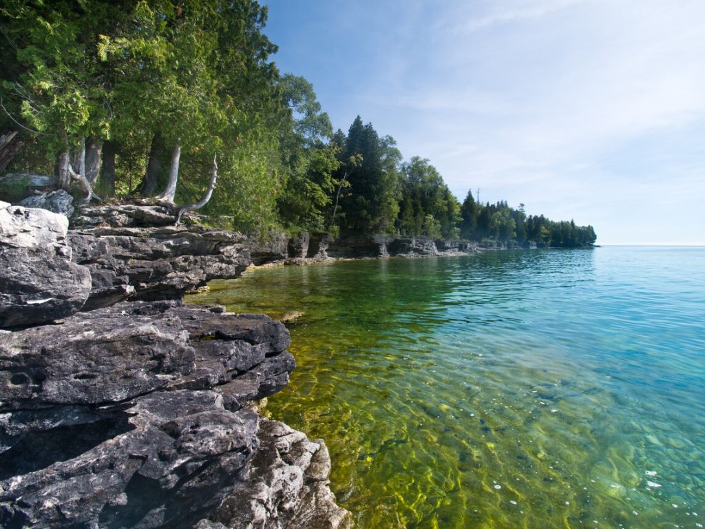 A rocky tree-lined shoreline with clear blue-green water in Door County, Wisconsin