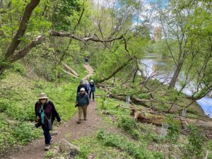 People walking up a hiking trail in a forested area along a body of water