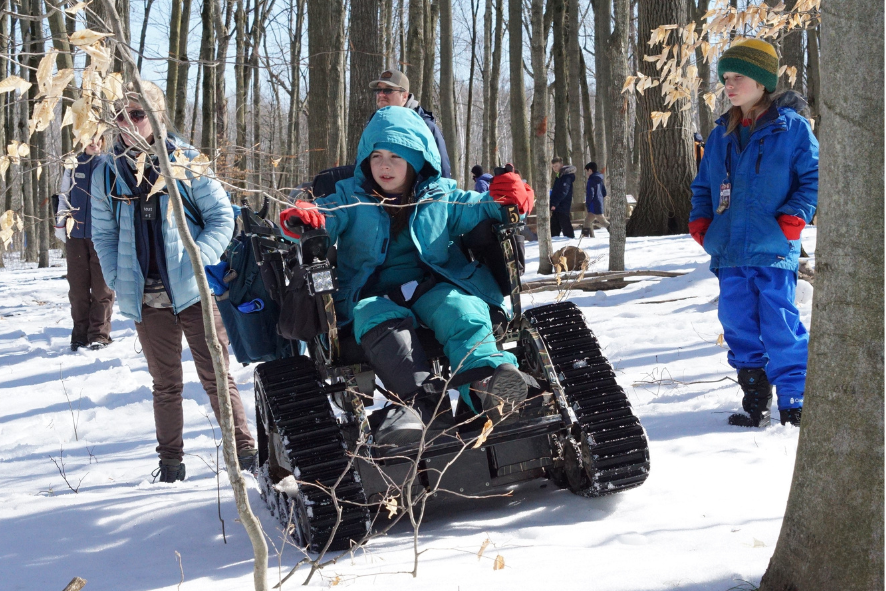 Blog Post Photo Dimensions 43 (24) Child using an all-terrain wheelchair in the woods duringn winter; photo for Diversity in the Outdoors blog