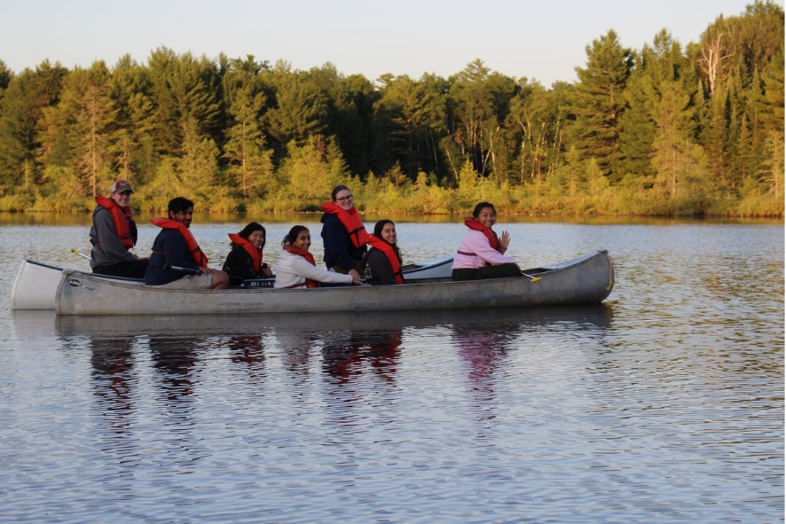 Seven students wearing life jackets on a canoe together smiling at the camera