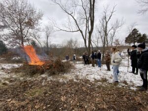 2023 grants for conservation and environmental education feature of students standing outside in the winter while burning a pile of brush.