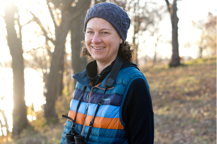 Kim Kreitinger smiling while standing in a sunny, lightly forested park