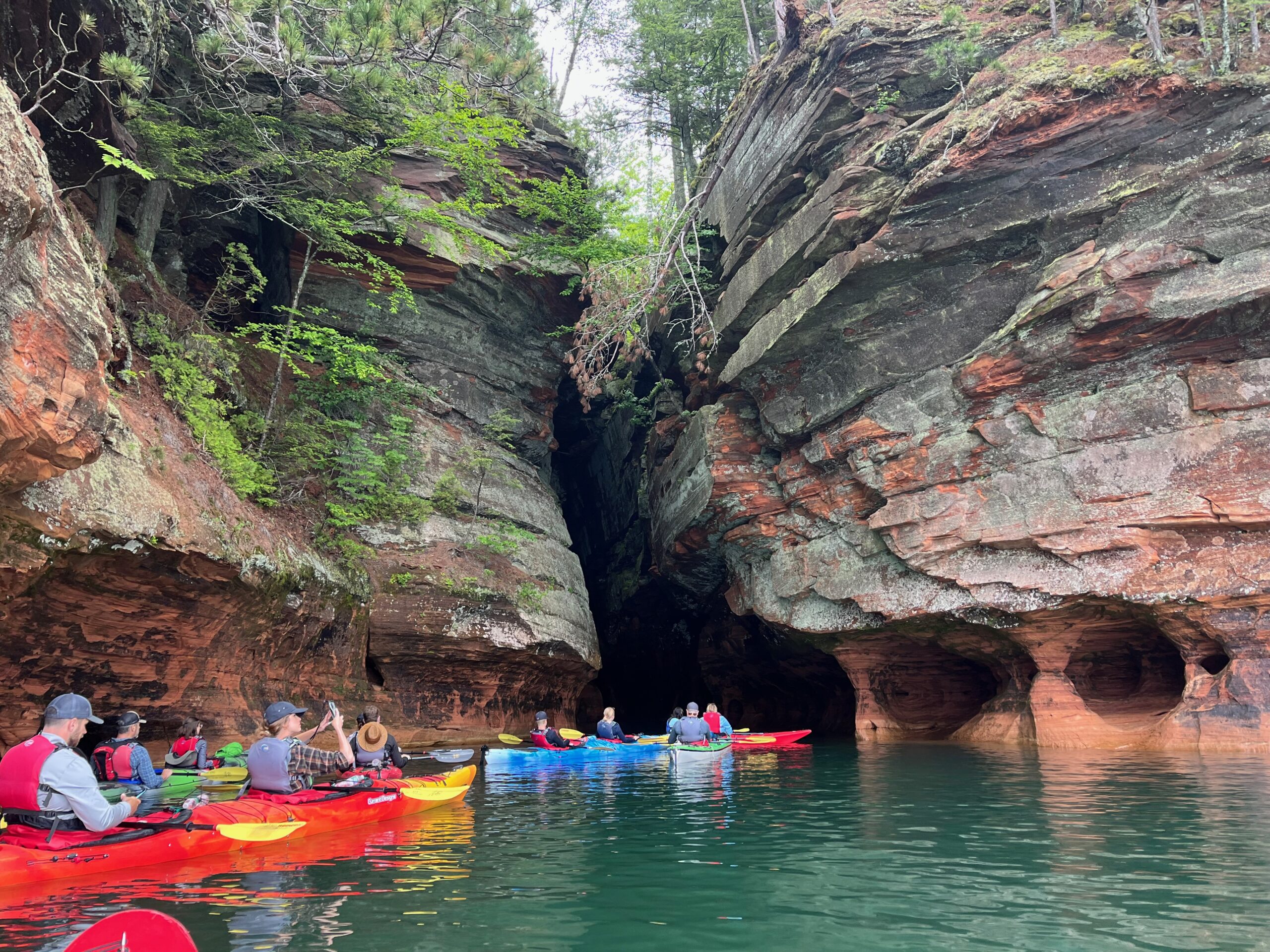 People kayaking next to large rock formations overhead